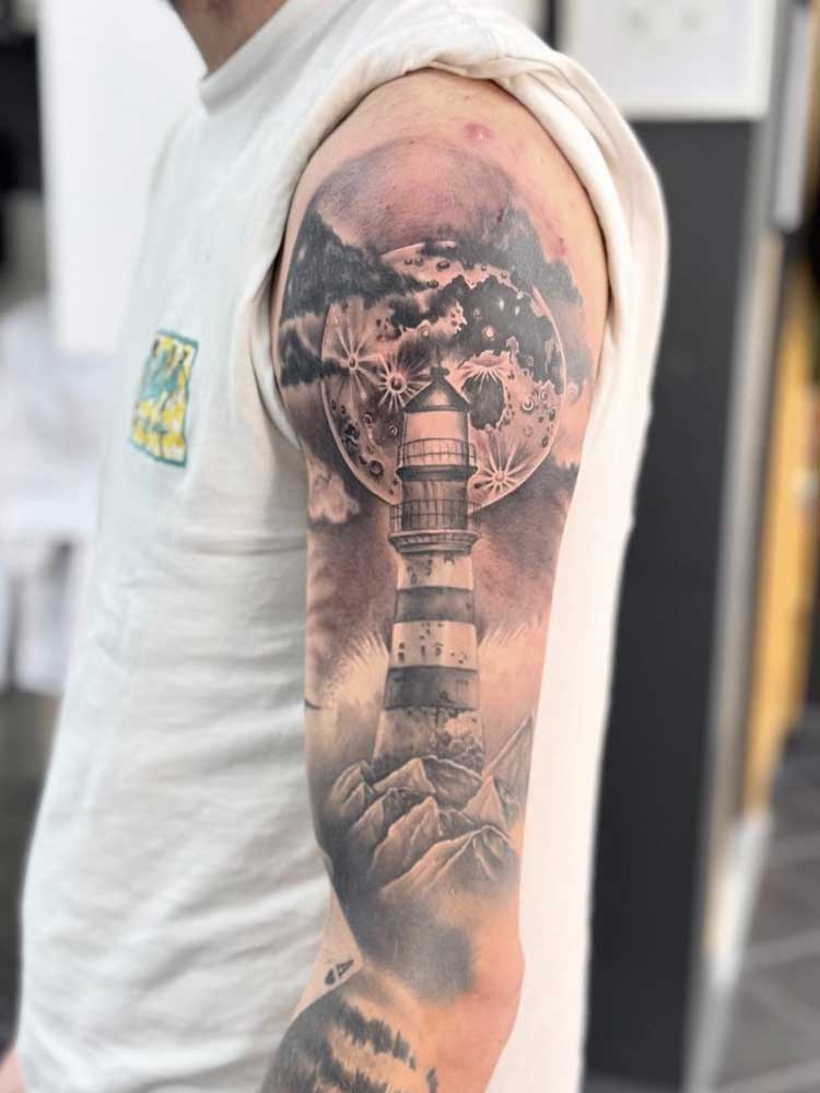 Tatuaggio con faro su una roccia e luna sullo sfondo